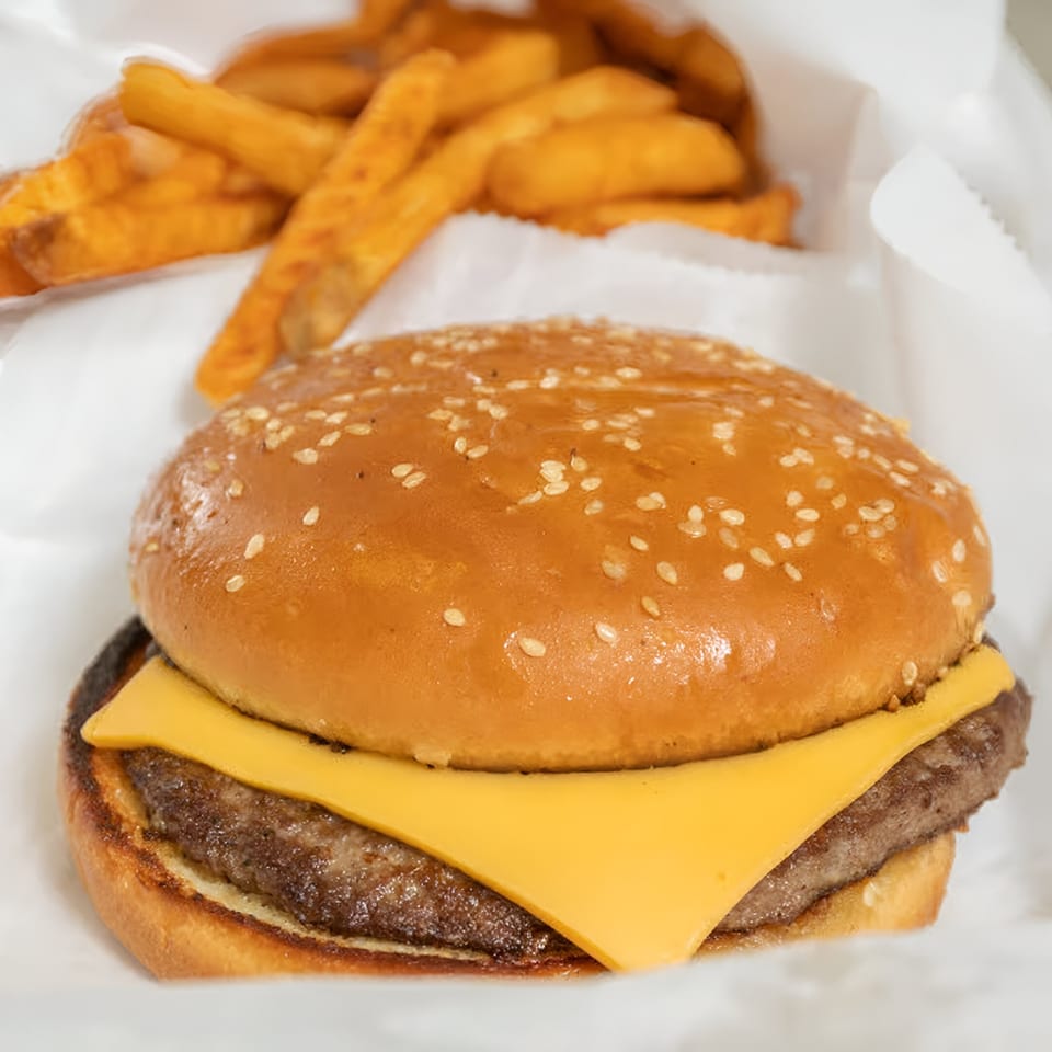 A cheeseburger with a sesame seed bun and a side of golden-brown french fries in white paper.