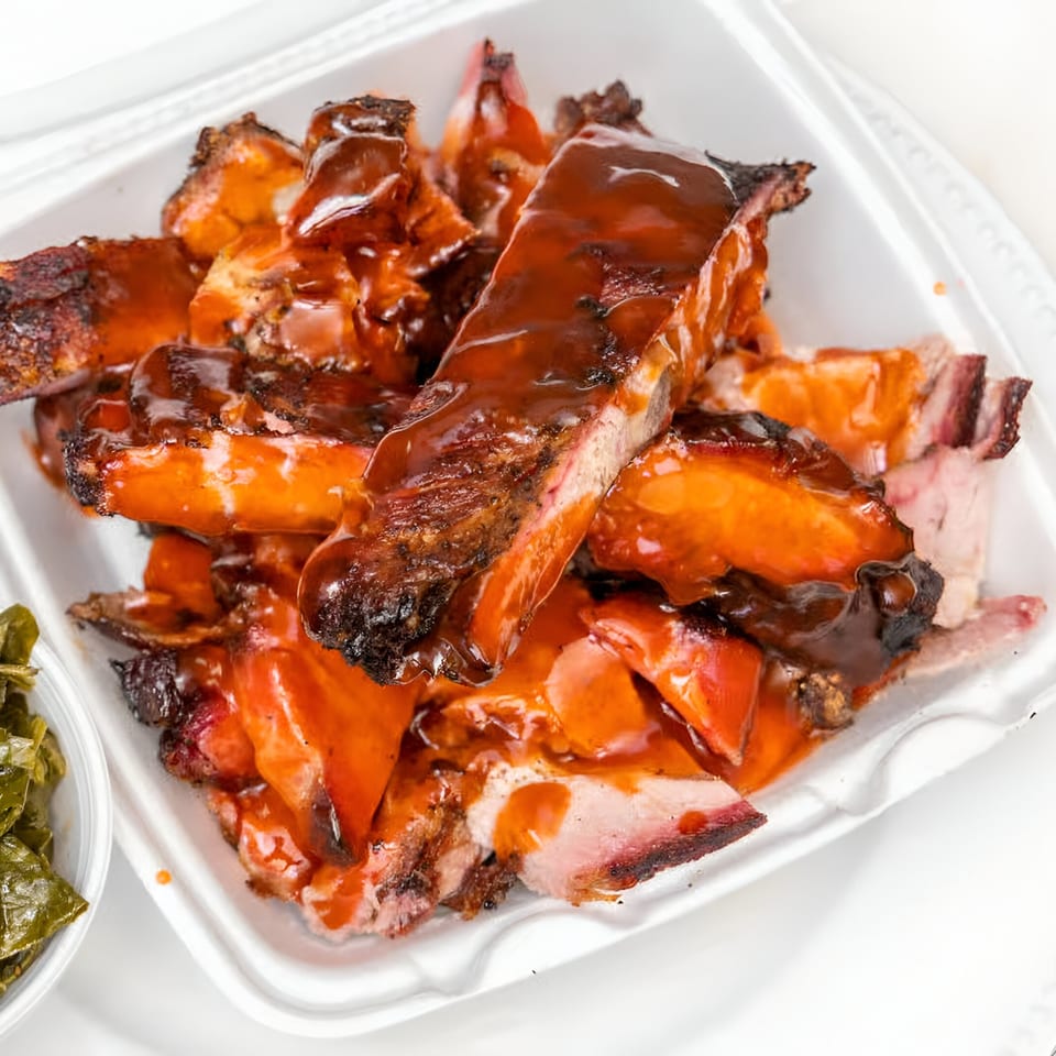 Ashley's Bar-B-Que ribs and chopped pork covered in sauce, with a side of collard greens.