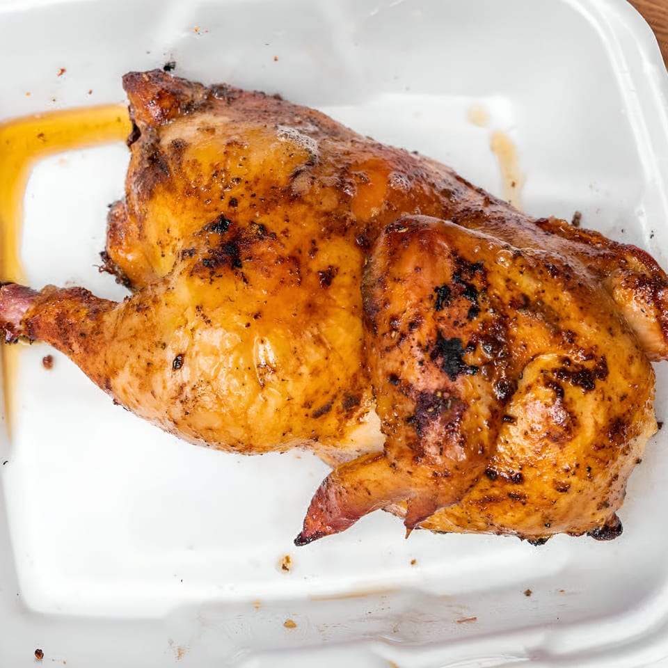 Ashley's Bar-B-Que's golden-brown roasted chicken, glistening with juices, in a white takeout container.